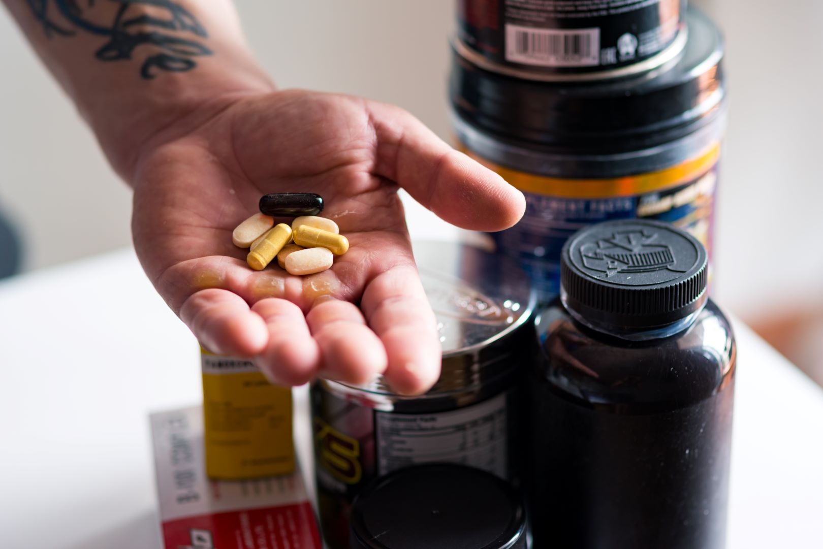 Hand holding assorted men’s health supplements with supplement containers in the background.